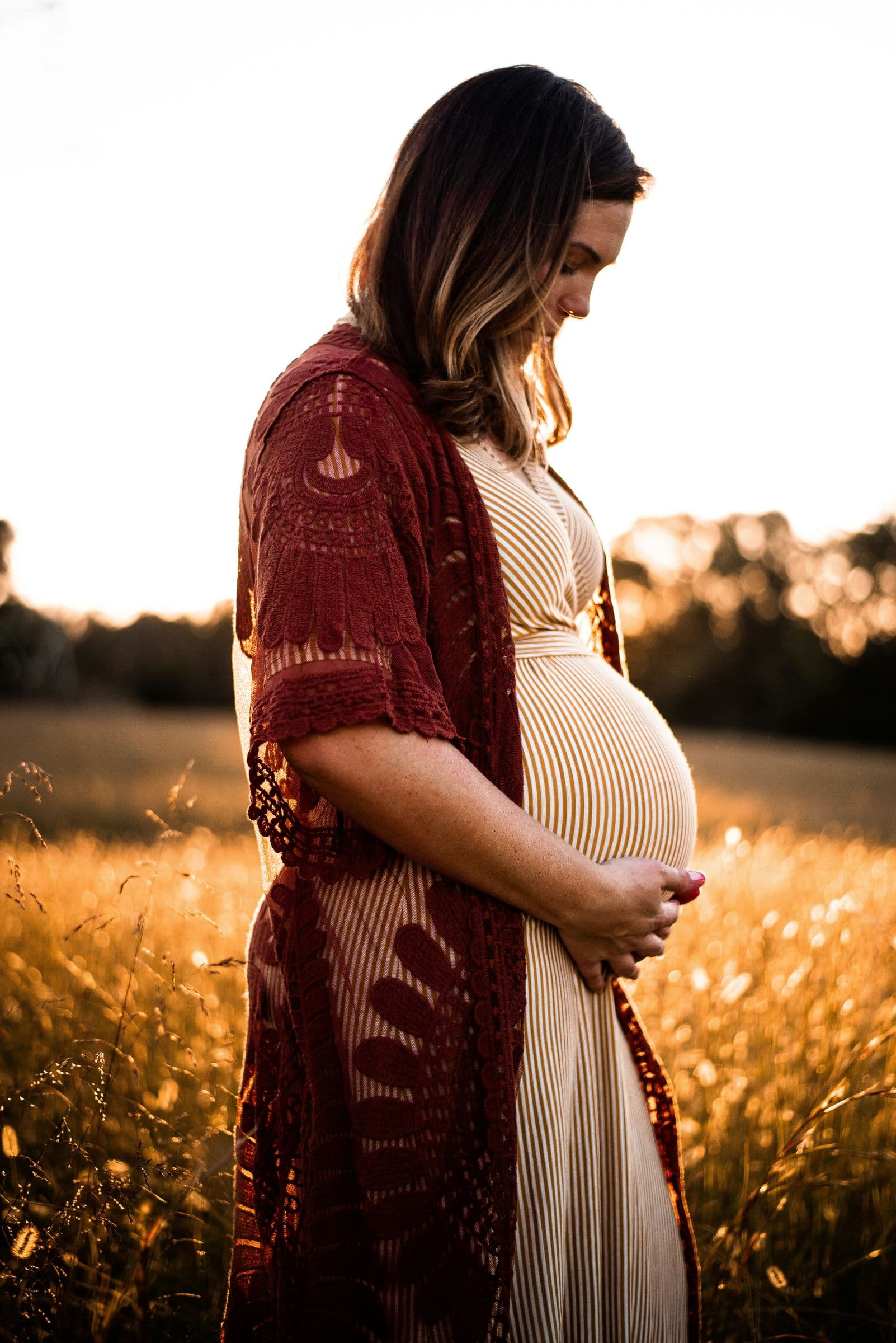 An expectant mother in a golden field at sunset